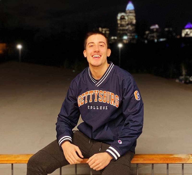 A picture of Tsvetmir sitting on a railing wearing a Gettysburg College jacket smiling at the camera